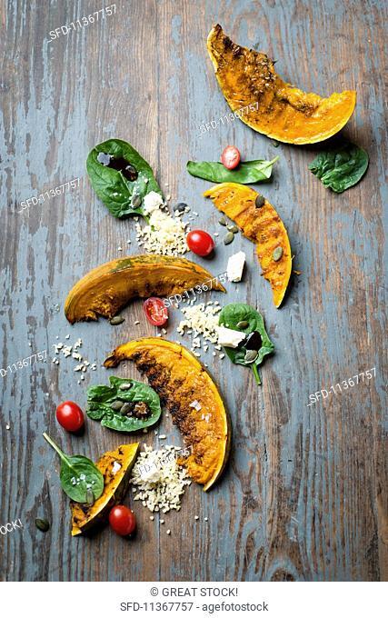 Grilled pumpkin wedges with a bulgur and spinach salad and feta cheese and wooden surface