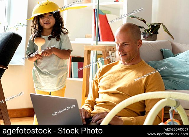 Cute girl playing with kitchen tools while father working from home