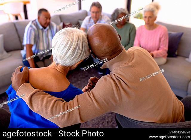 Rear view of multiracial senior man embracing woman in group therapy session at nursing home