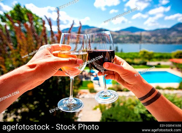 Okanagan Valley wine tasting tour, wineries visit during summer and spring vacations concept, man and woman hands toasting red and white wine glasses