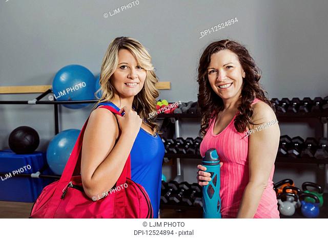 Two attractive middle-aged women posing for the camera after working out at a fitness class in a gym; Spruce Grove, Alberta, Canada
