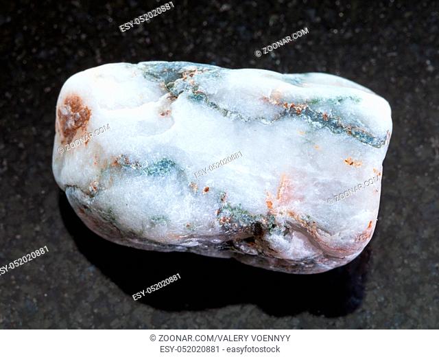 macro shooting of natural mineral rock specimen - tumbled marble piece on dark granite background from Greece