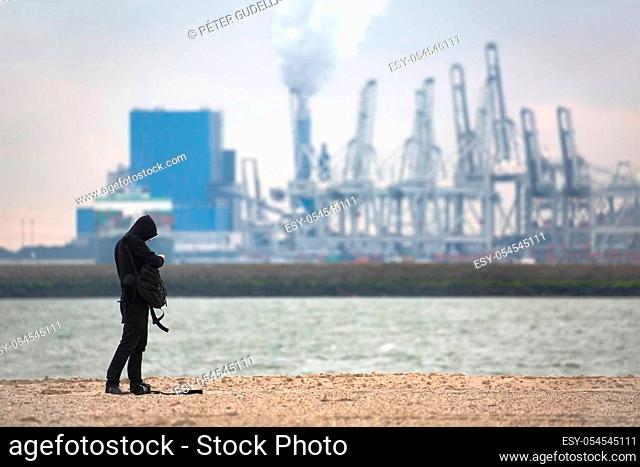 Photographer standing in front of power plant ang huge gantry cranes in the distance, smoke rising. Port area of Rotterdam, Maasvlakte