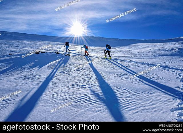 Austria, Tyrol, Sun shining over three skiers traveling through snow in Kitzbuehel Alps