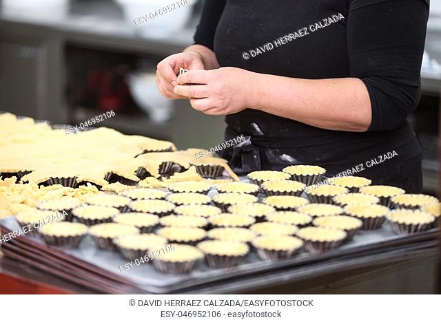Pastry chef making tartlets, putting the dough in baking dishes, at kitchen of pastry shop