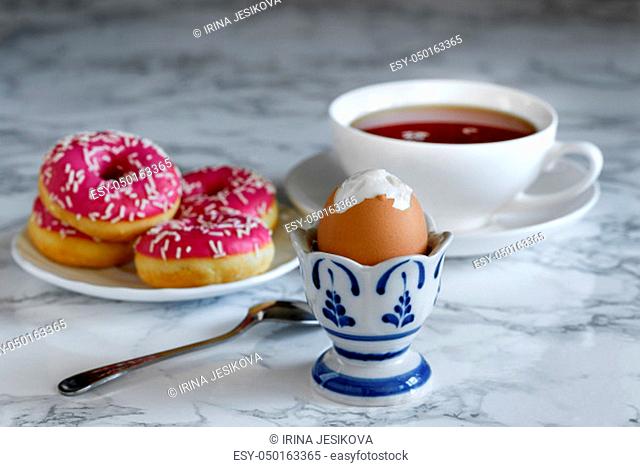 Boiled egg with tea and donuts in the background, breakfast time