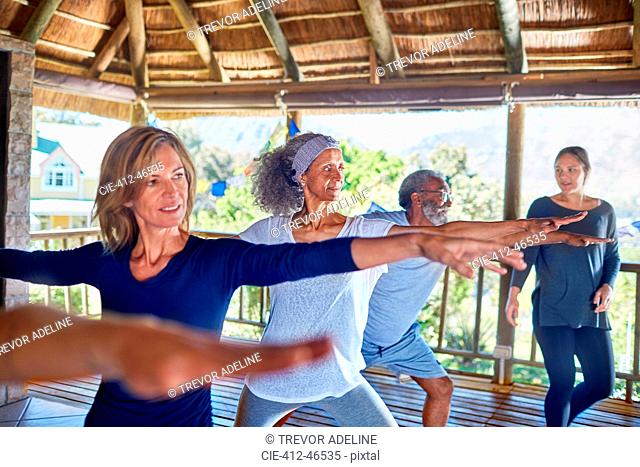 Yoga class practicing warrior 2 pose in hut during yoga retreat