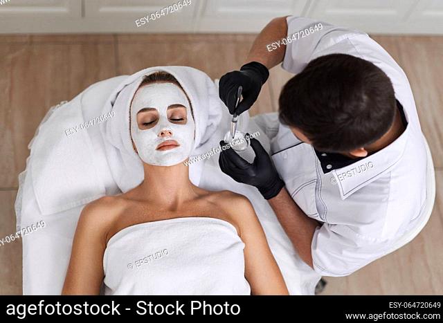 male beautician applies the mask to the face of beautiful woman in the spa salon. facial skin care concept