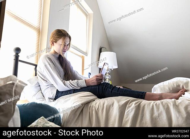 Teenage girl sitting on her bed using her smart phone