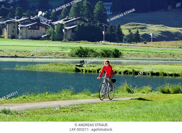 Woman cycling along Lake Champfer, Silvaplana, Upper Engadin, Canton of Graubuenden, Switzerland