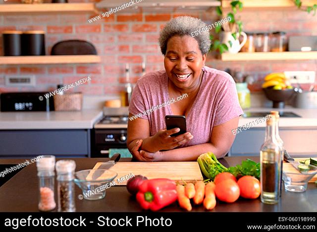 Happy african american senior woman using smartphone it kitchen