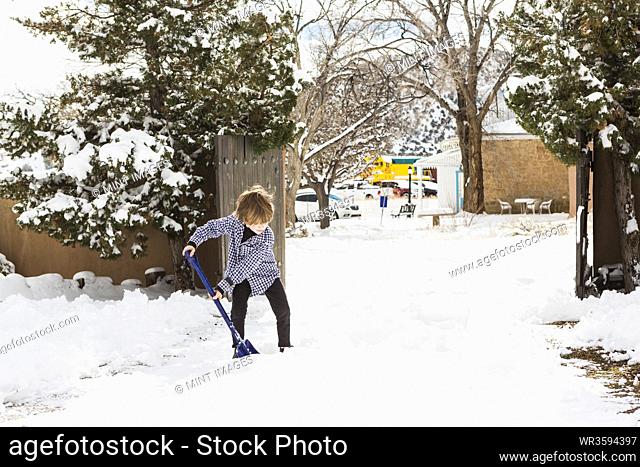 A six year old boy shoveling snow in driveway