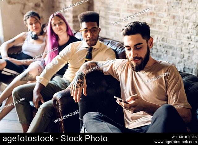 Group of friends sitting on sofa in a loft with smartphone