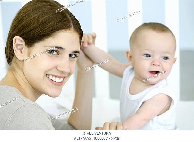 Mother holding baby's hands and smiling at camera