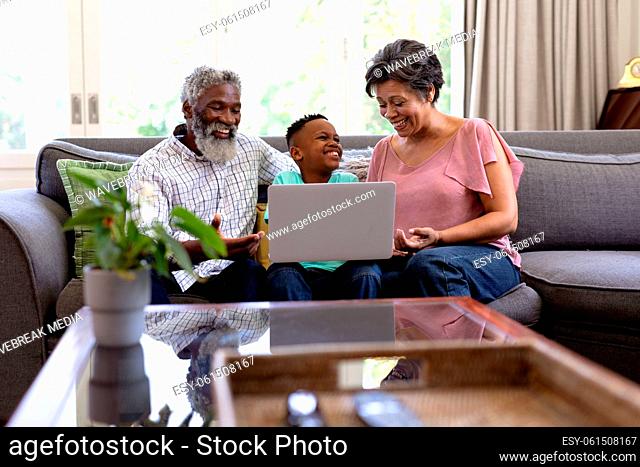 Mixed race boy and his grandparents using a laptop sitting on a couch