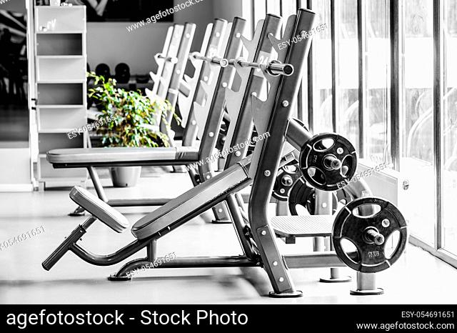 Modern gym interior with bench press equipment in a row, almost monochrome version