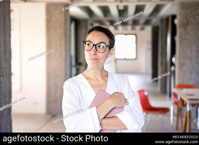 Mid adult woman with digital tablet looking away while standing at office