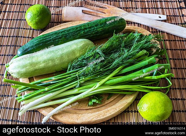Cucumber, zucchini, greens, limes and a cutting board lie on the kitchen table