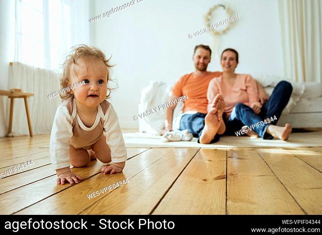 Cute girl crawling while mother and father sitting on floor at home