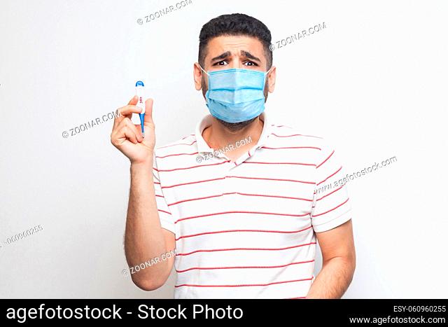39 degress. Scared panic worry sick man with surgical medical mask standing, holding thermometer are shoched for high temperature, looking at camera