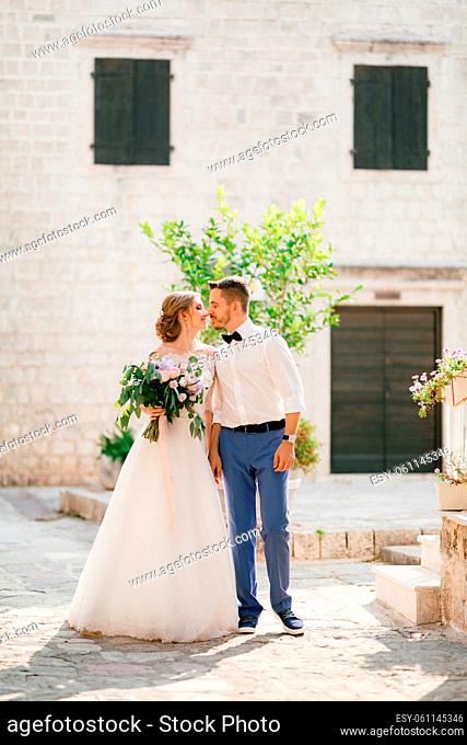 The bride and groom stand holding hands and kissing near a beautiful brick house in the old town of Perast, close-up. High quality photo