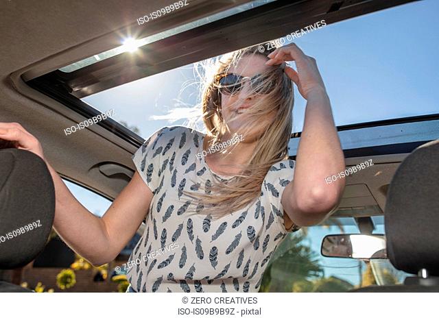 Young woman in car, looking out of open sun roof