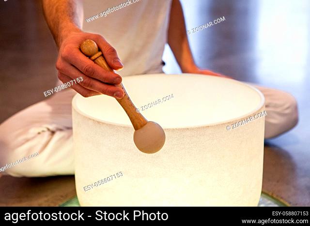 Man sitting in indian with his two big crystal bowls and his native sacred drum, playing sacred music in a meditative state. Closeup shot on one bowl