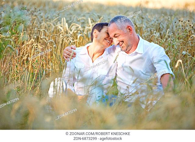 Zufriedenes Paar Senioren im Urlaub sitzt im Sommer in einem Feld voller Weizen
