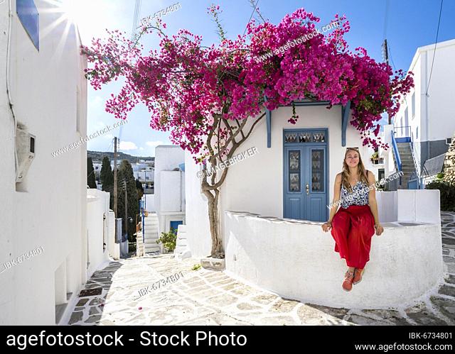 White-blue houses with blooming purple Bougainvillea (Bougainvillea), Young woman with red dress in the old town of Lefkes, Paros, Cyclades, Greece, Europe