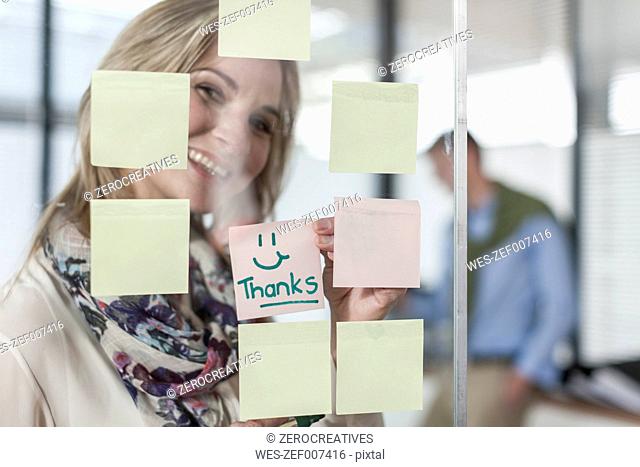 Woman in office writing thanks on sticky note