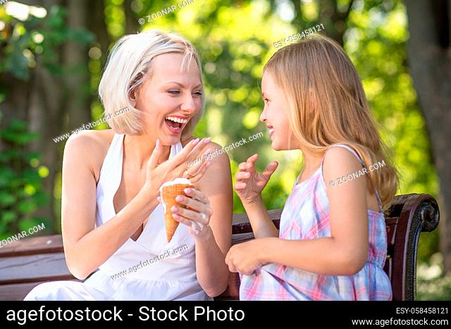 Mom and daughter eating ice cream together. Young mother laughing, holding ice cream