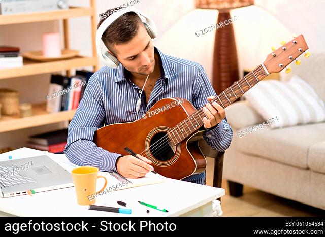 Portrait of handsome man playing guitar at home. Professional musician writing music for his concert