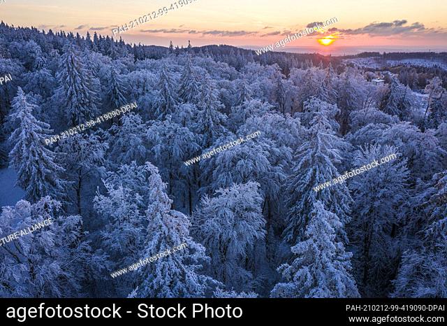 12 February 2021, Hessen, Sandplacken: The sun sets behind the trees covered with snow and ice at the Feldberg in Taunus (aerial view with a drone)