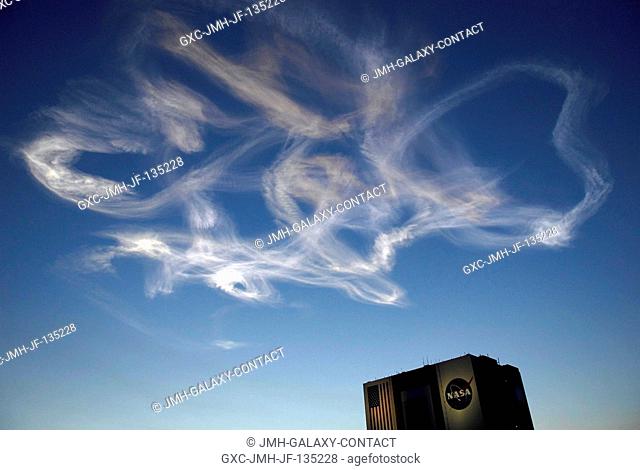 The drifting smoke plumes from the launch of Space Shuttle Atlantis (out of frame) swirl above the Vehicle Assembly Building near sunset
