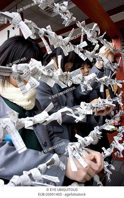 Asakusa Kannon or Senso-ji Temple. Three young Japanese female students hanging their omikuji folded fortune telling paper slips on bars outside the temple