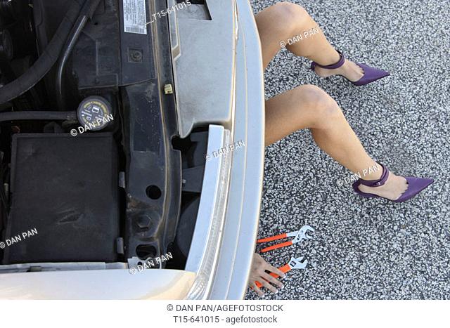 Woman in purple high heels getting under a car fixing it only show her legs, hands and tools
