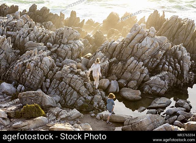 View from above of a teenage girl exploring rock pools at sunset on a beach, De Kelders, Western Cape, South Africa