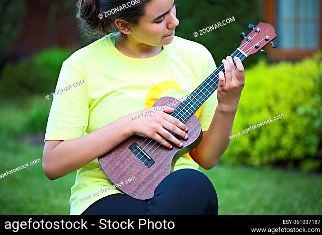 Cute teen girl playing her ukulele outdoors in the evening