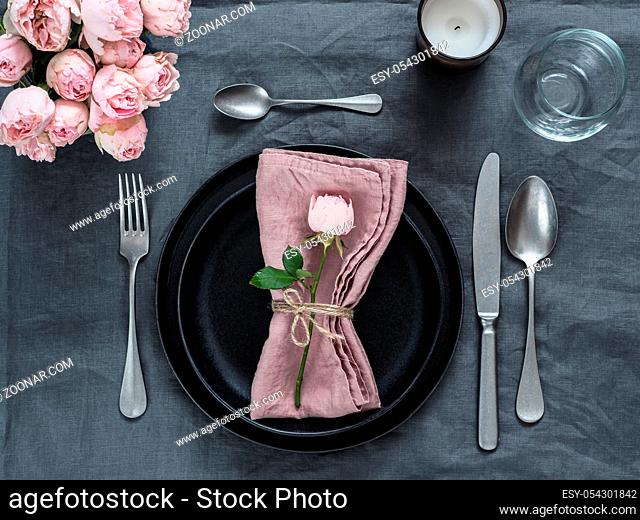 Beautiful table setting with candle on gray linen tablecloth. Festive table setting for wedding dinner with pink spray rose and pink napkin on plate