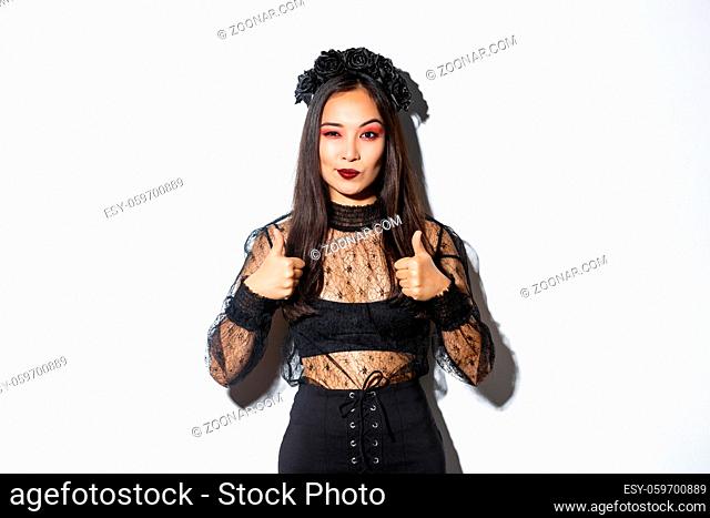 Pleased sassy attractive woman in witch dress showing thumbs-up in approval, like and praise your choice, making compliment, standing over white background