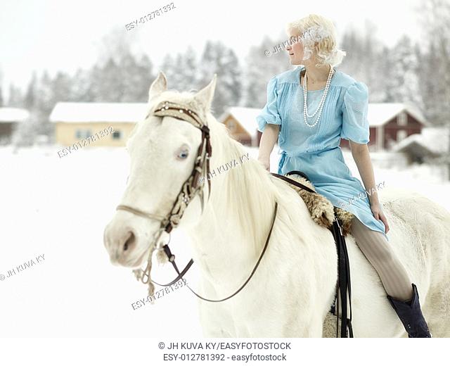 Attractive woman wearing blue dress and she riding a white horse. South Finland in February