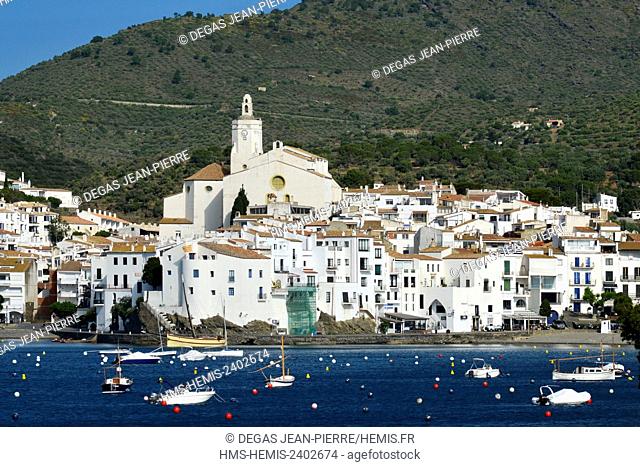 Spain, Catalonia, Costa Brava, province of Girona, Cadaques, wooden fishing boats in the middle of a bay with one city of white houses and a mountain in the...