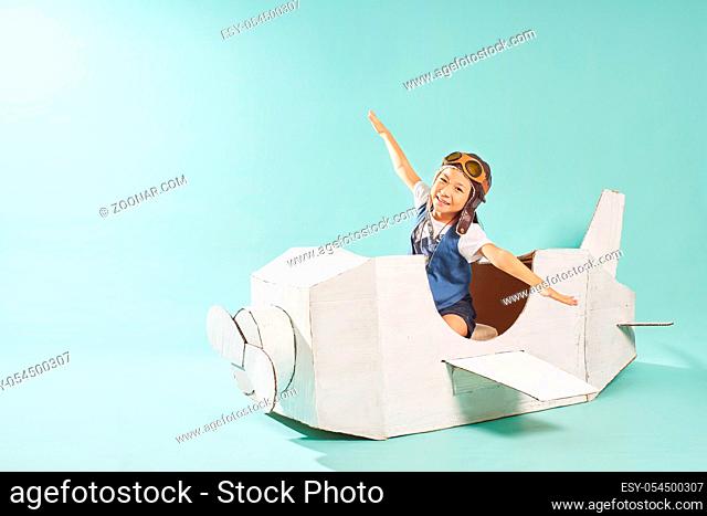 Little cute girl playing with a cardboard airplane. White retro style cardboard airplane on mint green background . Childhood dream imagination concept
