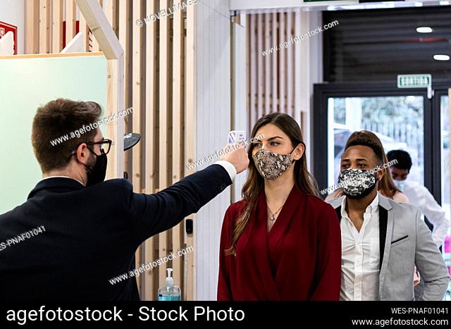 Man checking temperature of employees with face mask through infrared thermometer at office