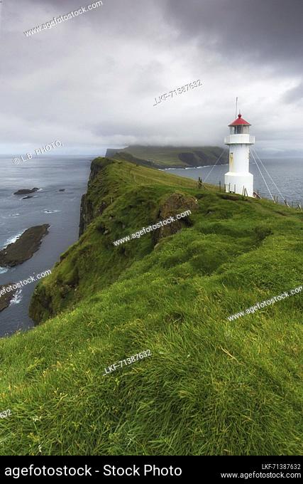 View of cliffs and Mykines Holmur Lighthouse up to Mykines, Faeroe Islands. Dark clouds
