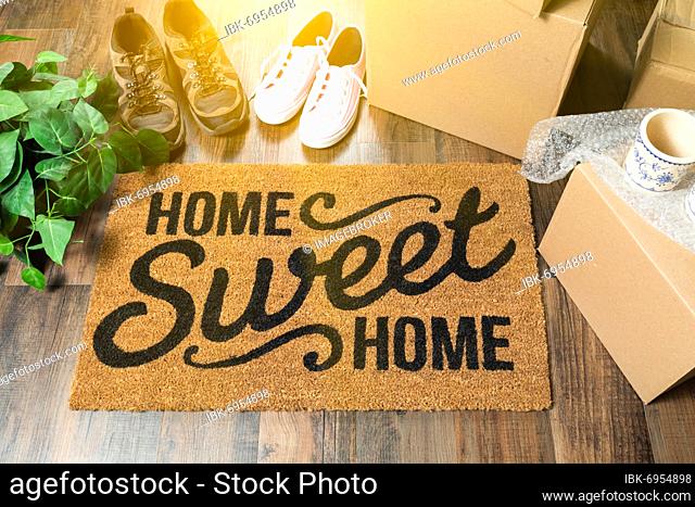 Home sweet home welcome mat, moving boxes, women and male shoes and plant on hard wood floors