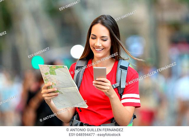 Front view of a happy teen tourist searching location online walking on the street