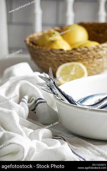 Fresh needle fish, sardines on the kitchen table, linen tablecloth, lemons and salt