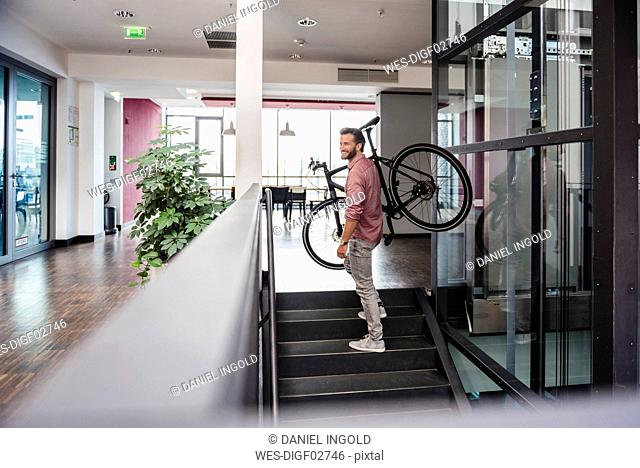 Man with bicycle walking upstairs in modern office