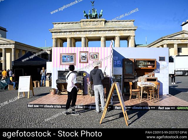 15 September 2023, Berlin: Passers-by look at a replica of a flood-damaged apartment in front of the Brandenburg Gate, which Greenpeace is using to protest for...